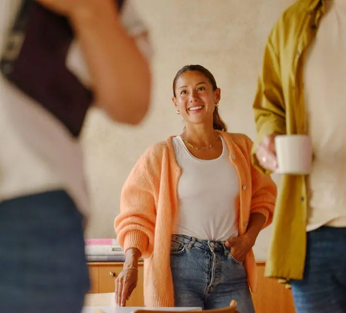 Une consultante souriante, une tasse a la main, entouree de collegues.